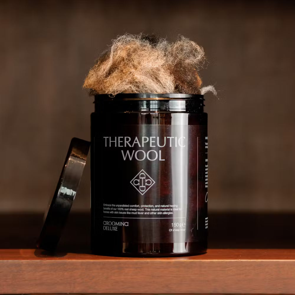 A jar labeled ‘Therapeutic Wool’ from Kentucky Grooming Deluxe sits on a wooden shelf with its lid off, showing natural sheep wool inside. The background is softly lit in warm brown tones, giving a luxurious, natural aesthetic