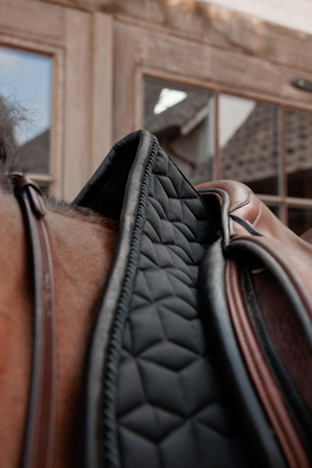 Close up of a black saddlepad under a brown saddle on a bay horse