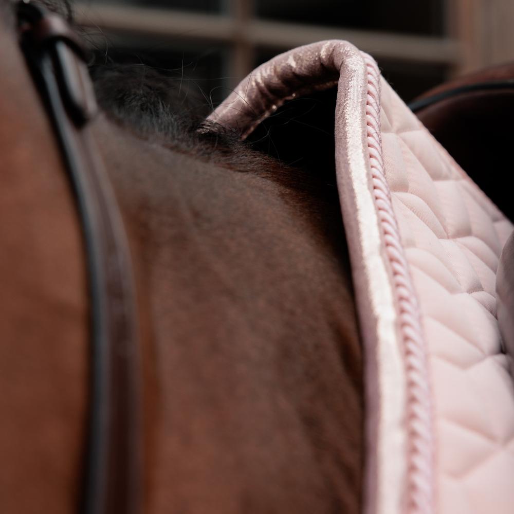 Close up of a pink saddlepad under a brown saddle on a bay horse