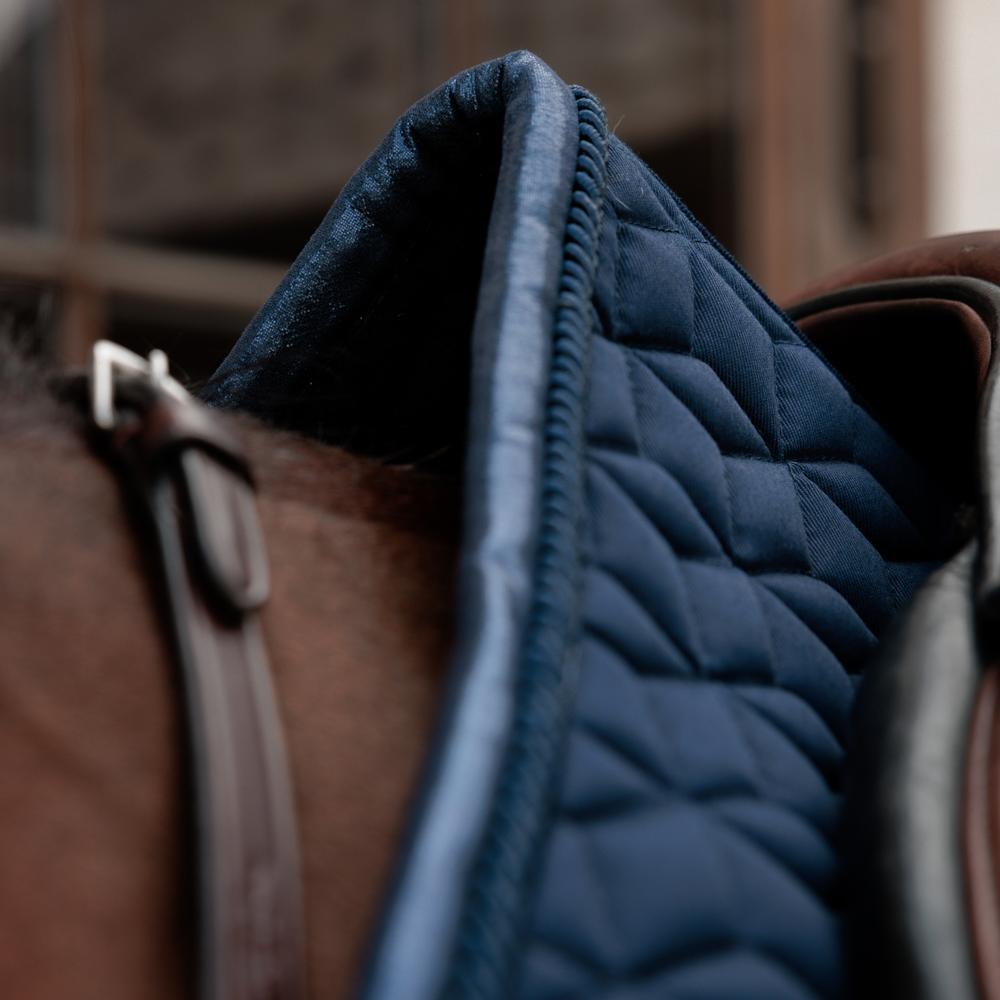 Close up of a navy saddlepad under a brown saddle on a bay horse