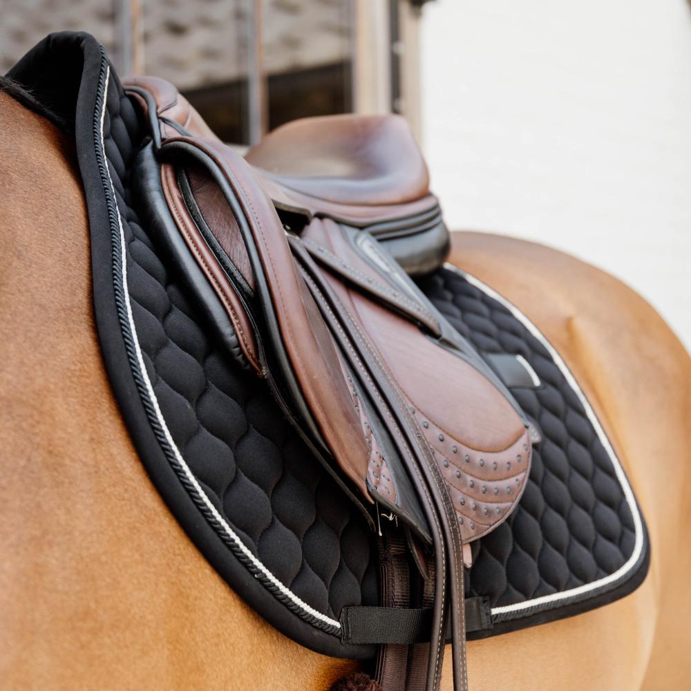 Black saddlepad under a brown saddle on a bay horse