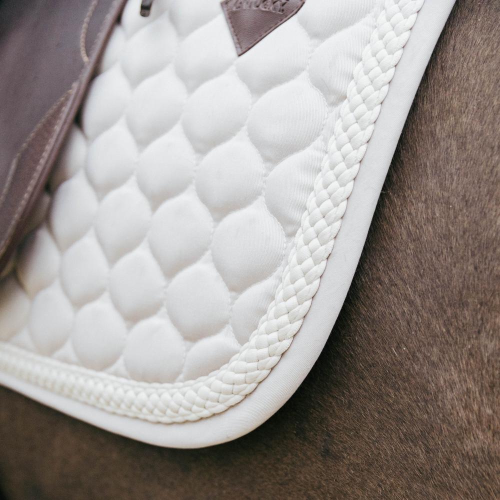 Close up of a beige saddlepad under a brown saddle on a bay horse