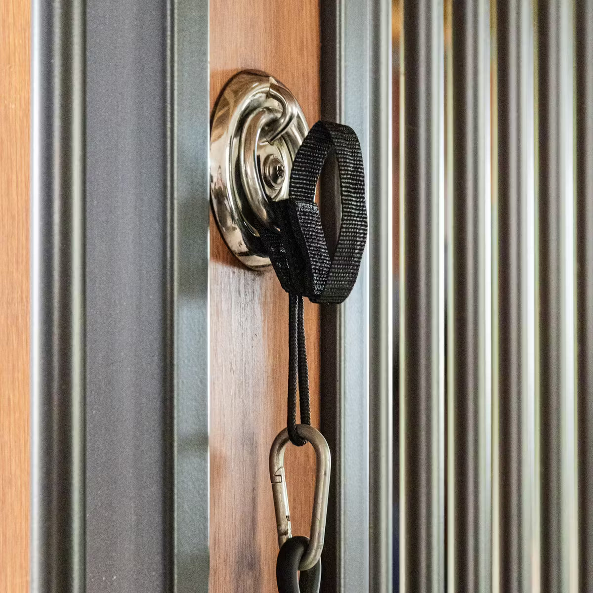 Close-up of a door handle with a black strap and carabiner on a wooden door.