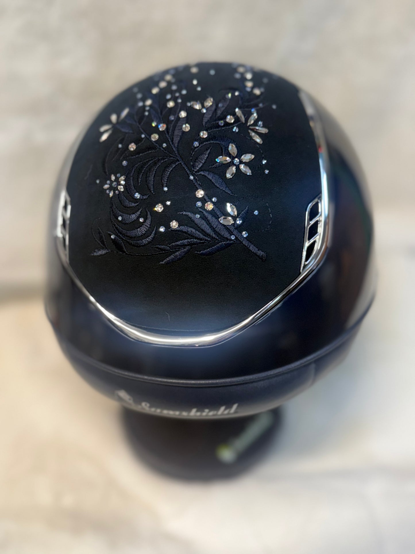 Navy decorative helmet with floral patterns and rhinestones on a neutral background