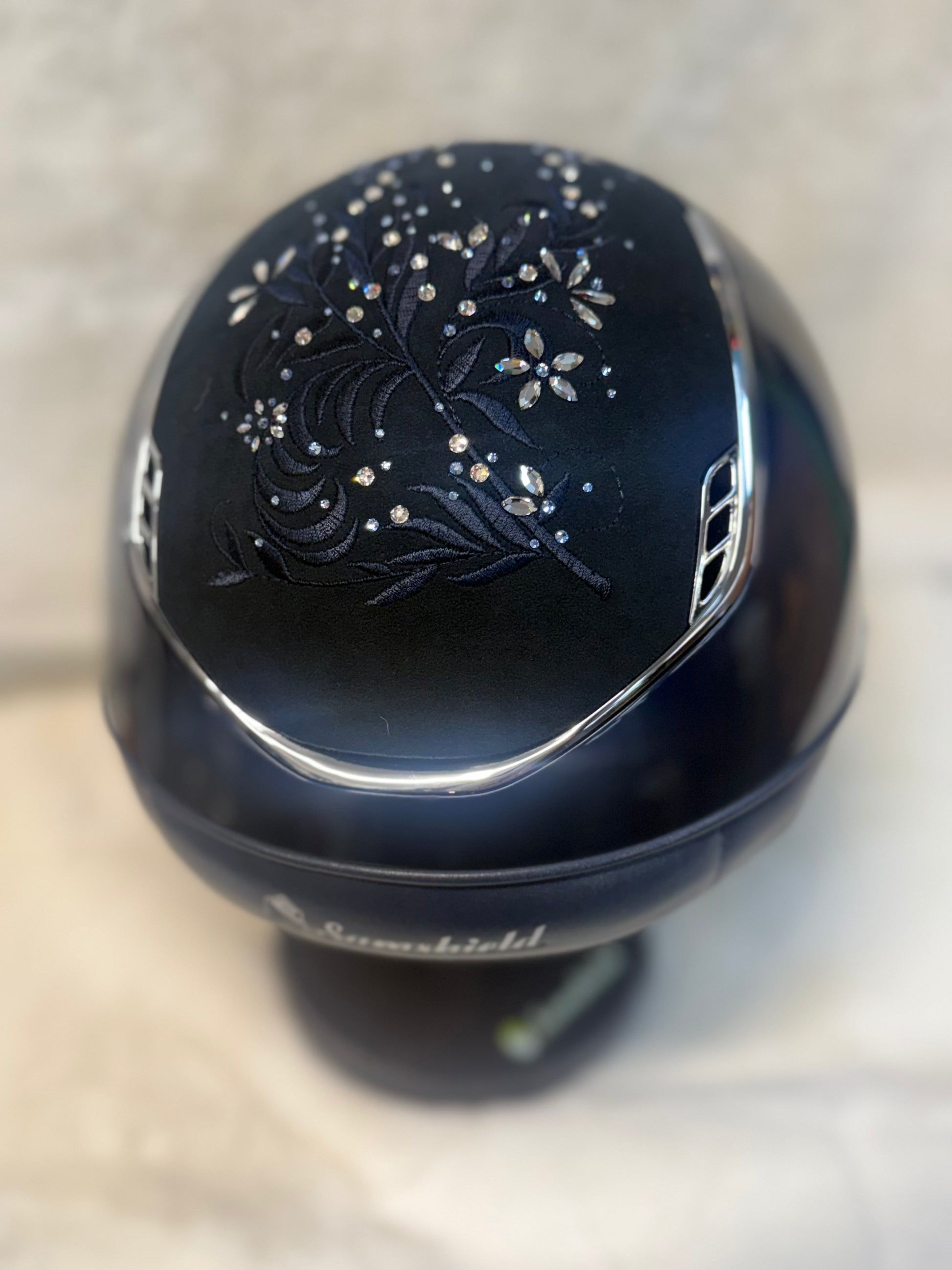 Navy decorative helmet with floral patterns and rhinestones on a neutral background