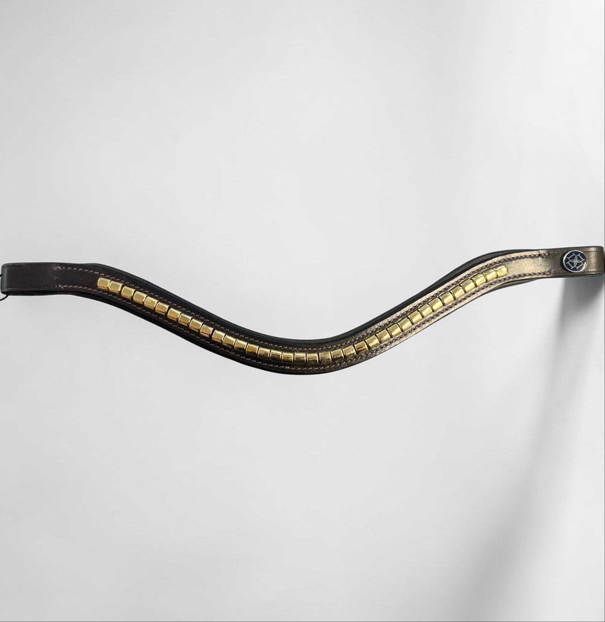 A browband with a wavy, S-shaped curve, featuring a row of gold-toned rectangular studs or metallic accents along the center and a small circular blue emblem near the bottom.