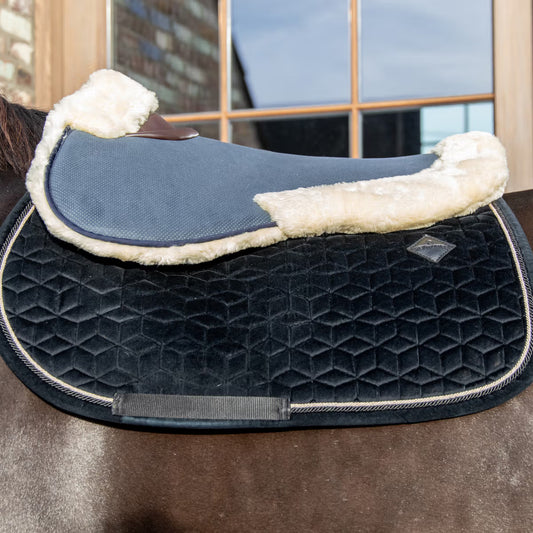 Equestrian saddle with blue pad and white fleece on a horse, blurred indoor background
