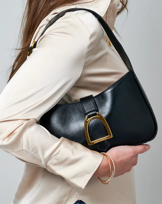 Person holding a black handbag with a gold buckle against a neutral background