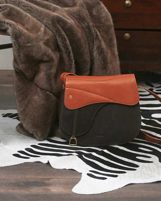 Equestrian saddle shaped handbag on a zebra print rug with a brown fur rug hanging off a chair behind it.