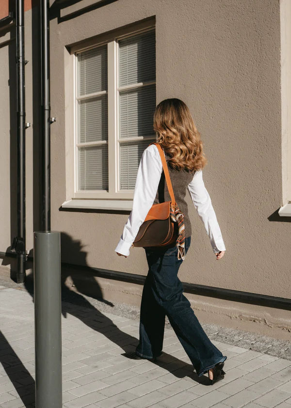 Equestrian saddle shaped handbag on the shoulder of a woman walking down the street
