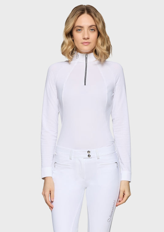 Woman wearing a white competition shirt and white breeches on a beige background