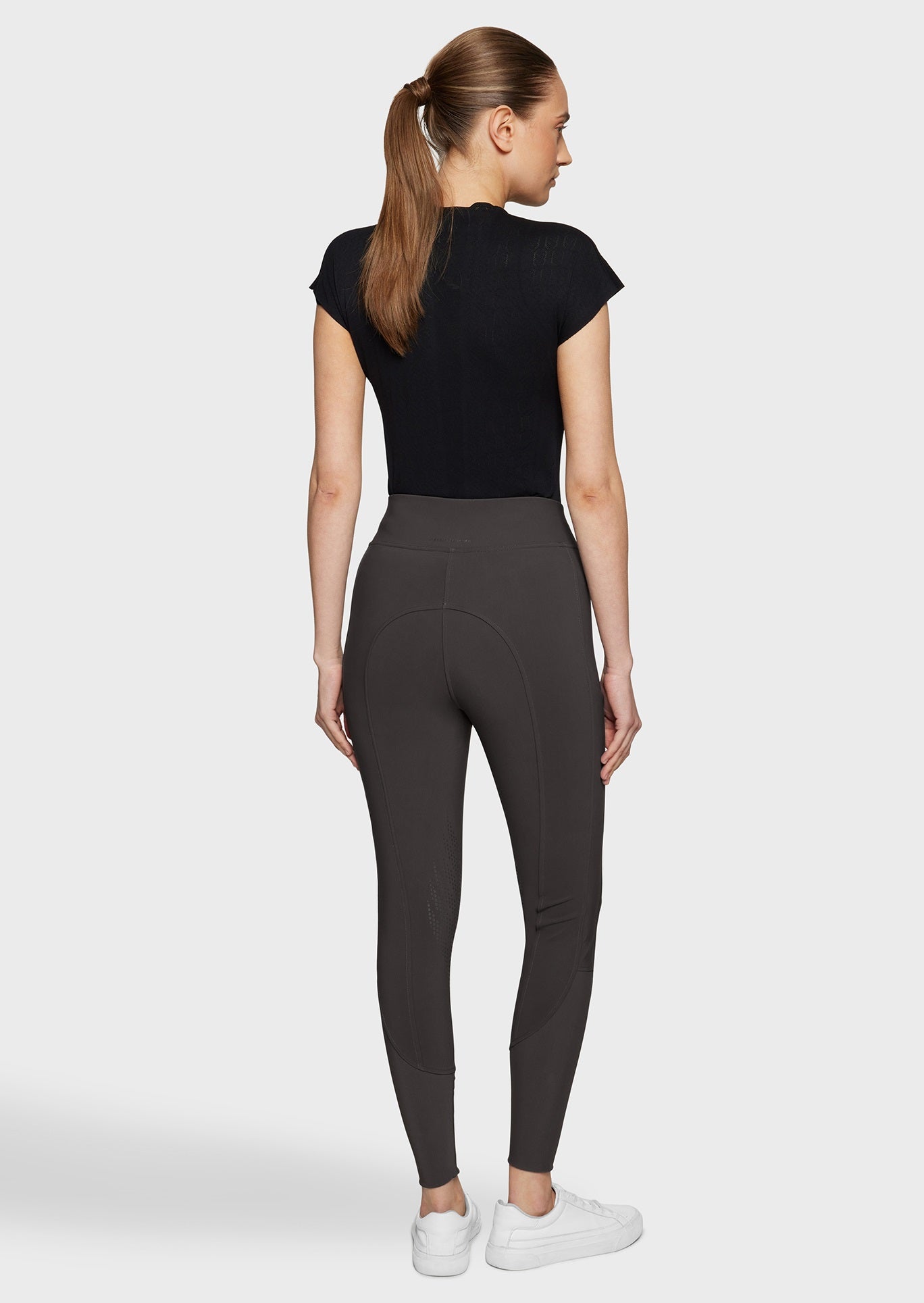 Woman wearing brown breeches and a black top on a beige background