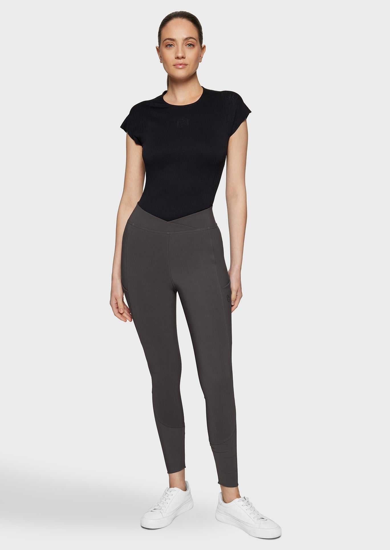 Woman wearing brown breeches and a black top on a beige background