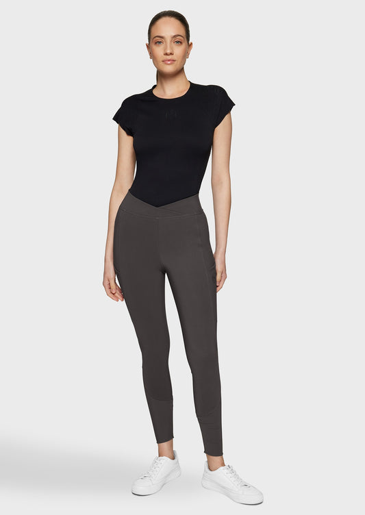 Woman wearing brown breeches and a black top on a beige background