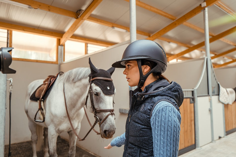 Person in equestrian gear standing next to a horse in a stable