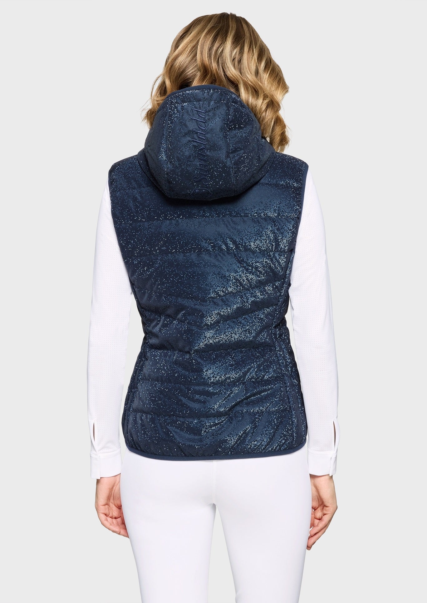 Woman wearing a sparkly navy gilet and white breeches on a beige background