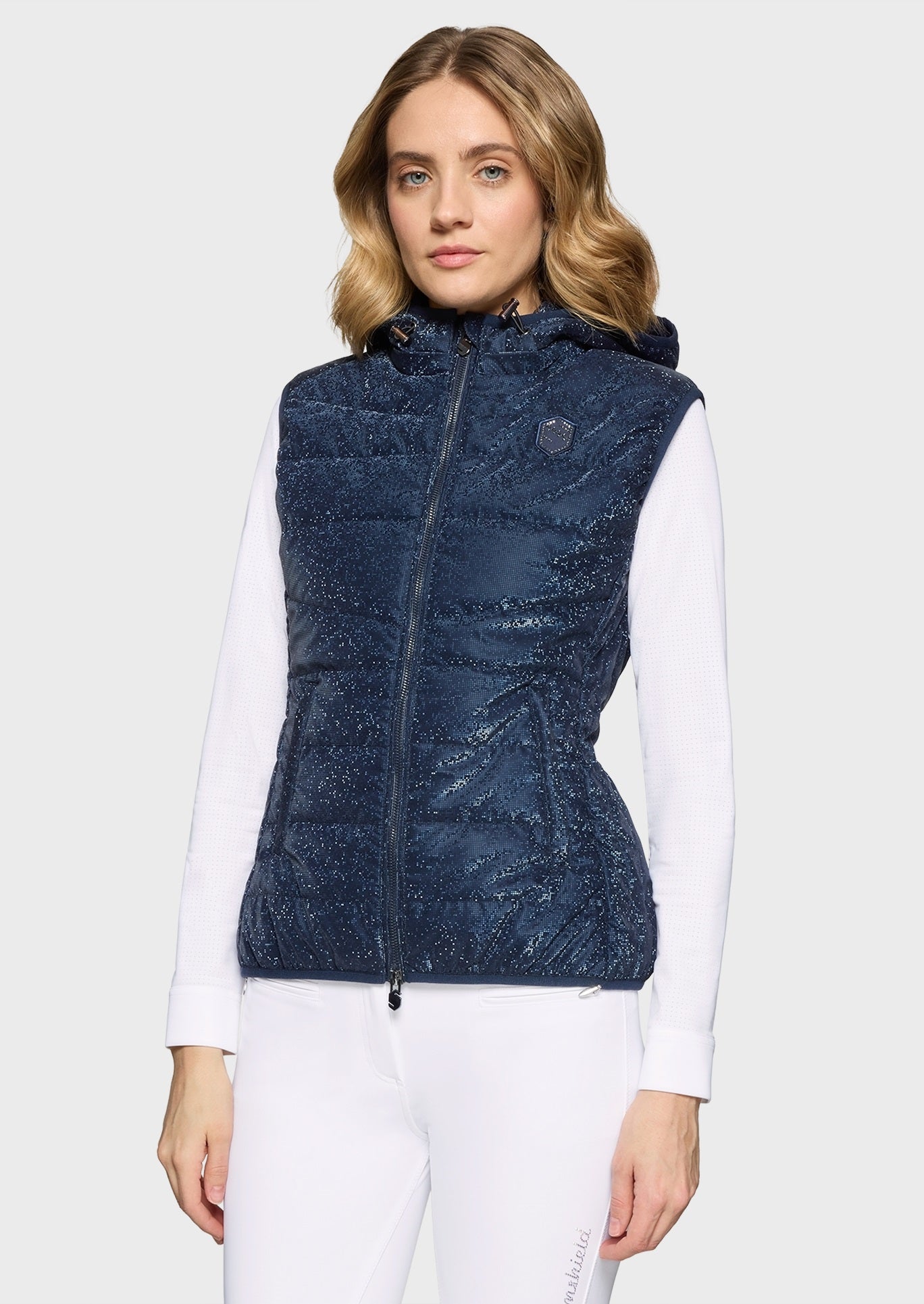 Woman wearing a sparkly navy gilet and white breeches on a beige background