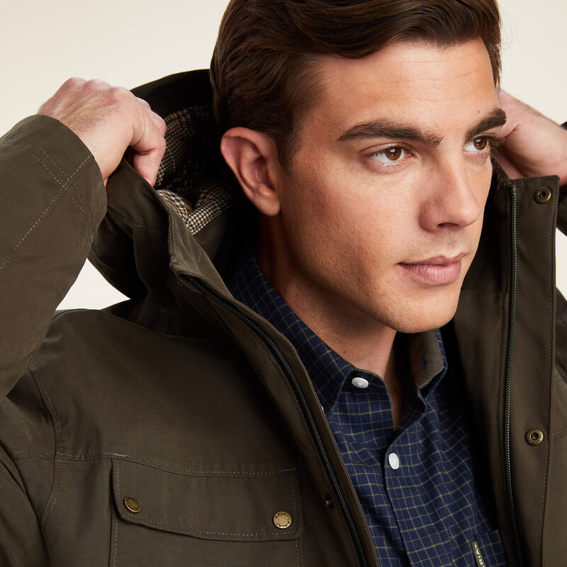 Man wearing a dark green jacket over a blue checkered shirt on a neutral background