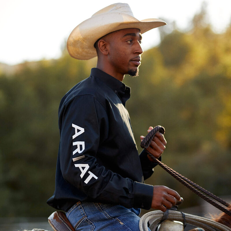 Man wearing an Ariat shirt holding a rope with a blurred natural background