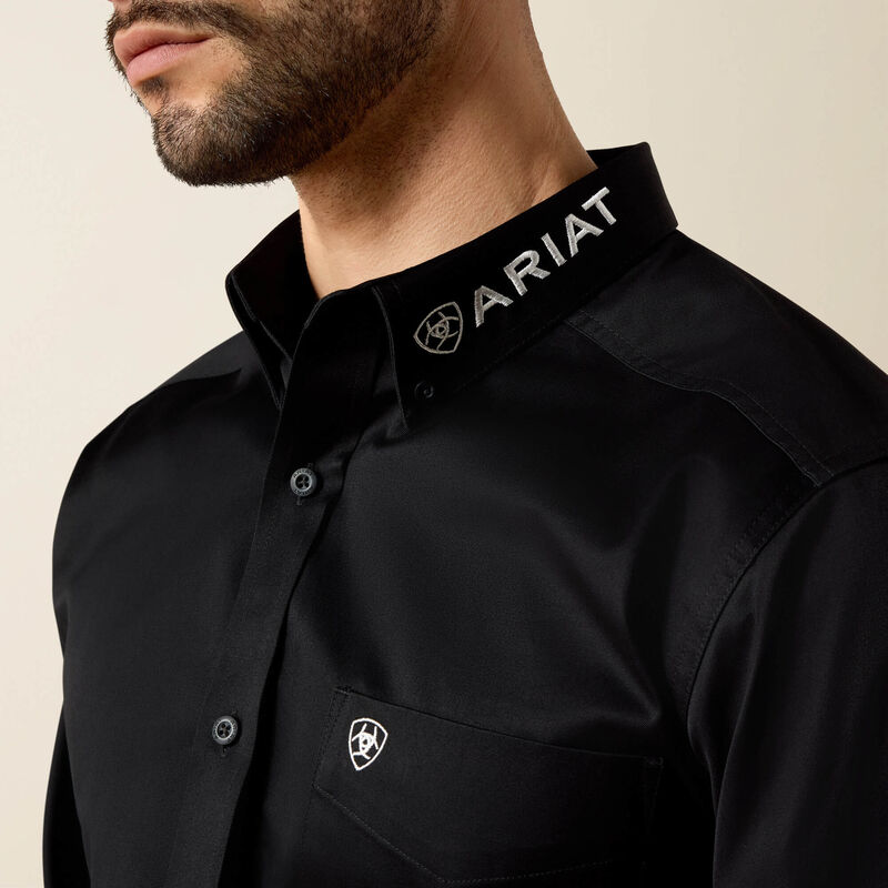 Black shirt with Ariat logo on collar and chest against a beige background