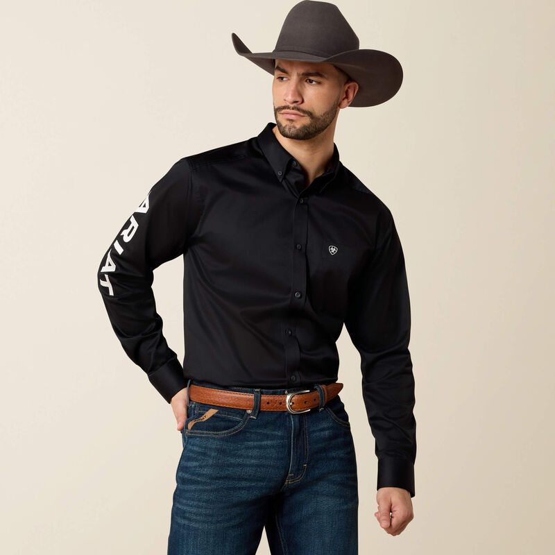Man wearing a black shirt with white text, blue jeans, and a brown cowboy hat on a beige background