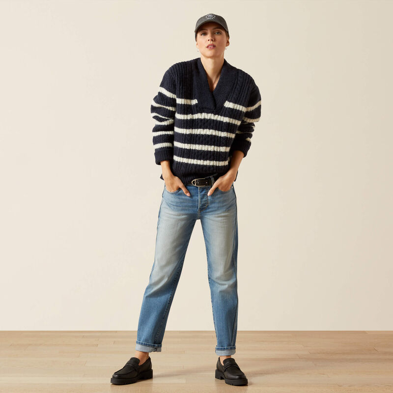 Person wearing a striped sweater, jeans, and cap on a plain background