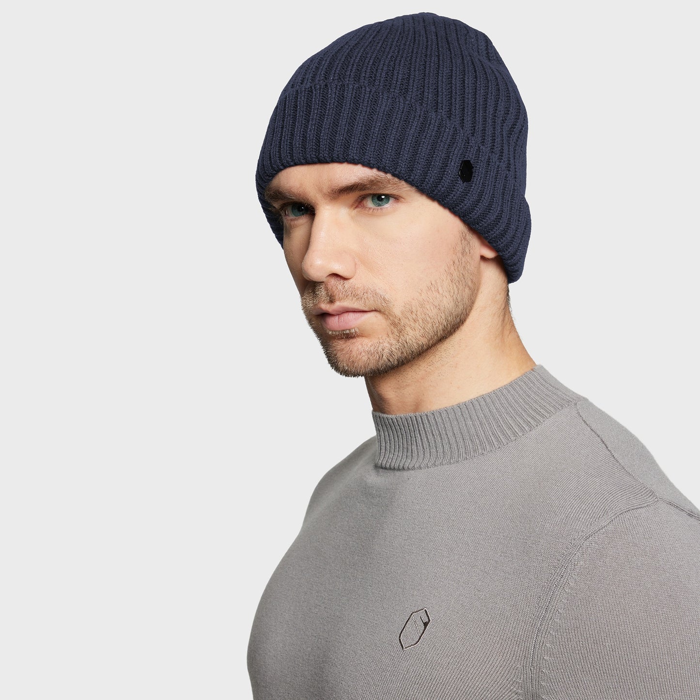 Man wearing a navy blue beanie and gray sweater on a light gray background