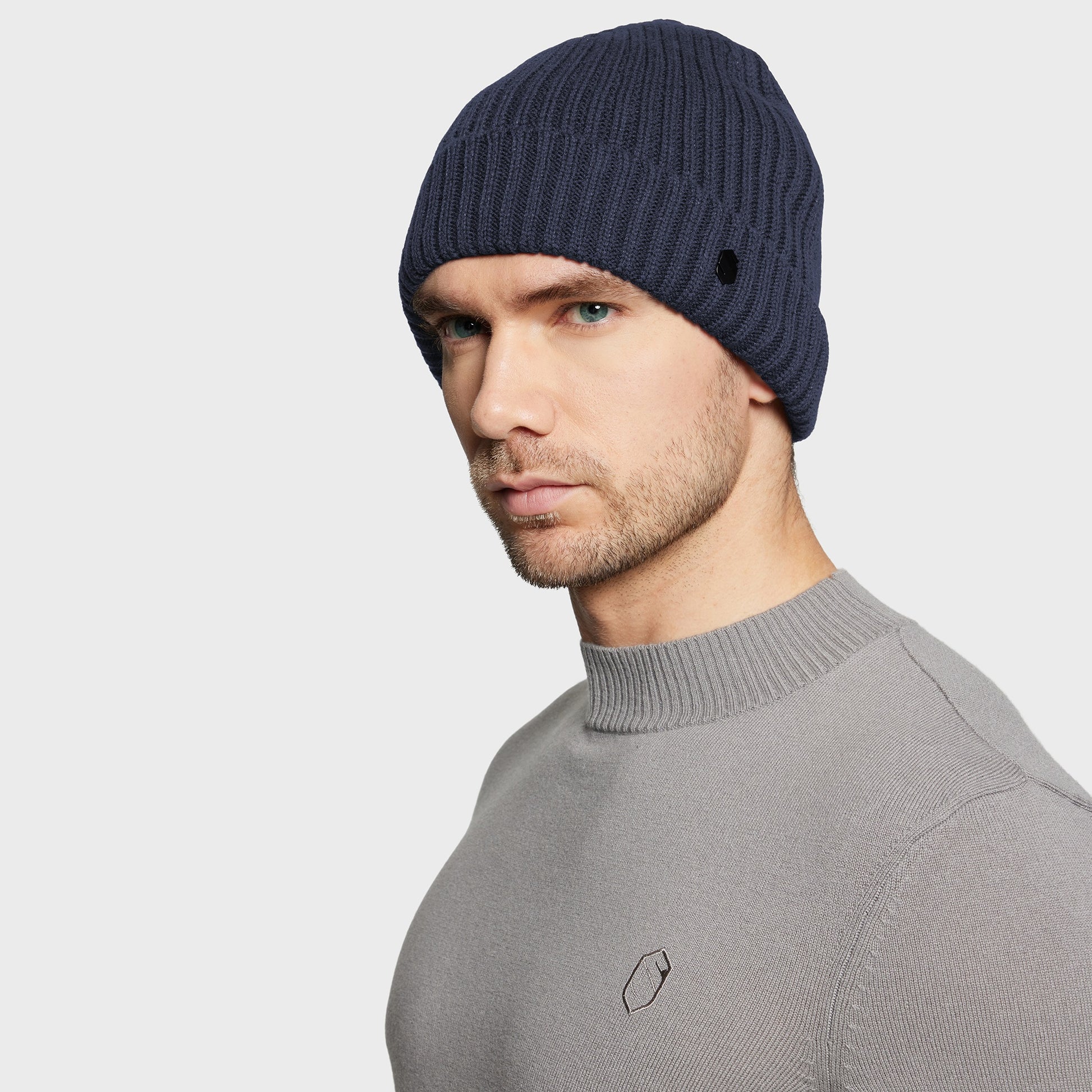 Man wearing a navy blue beanie and gray sweater on a light gray background