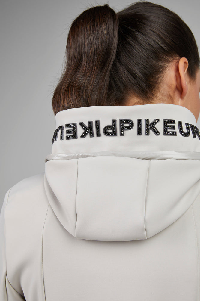 Person wearing a light gray hoodie with a brand logo on the hood against a gray background