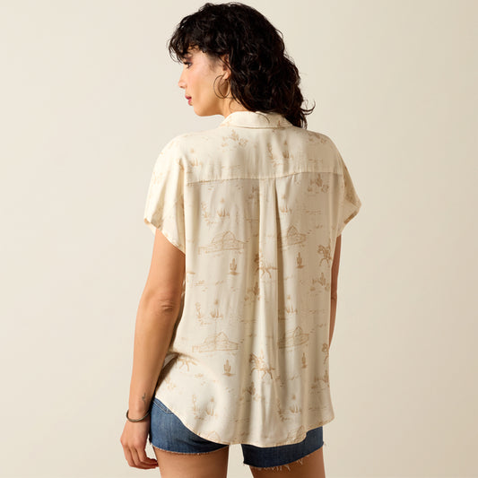 Woman wearing a beige patterned shirt and denim shorts on a plain background