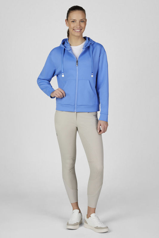 A woman modeling a bright blue zip-up hoodie with white drawstrings, paired with beige leggings and white sneakers, against a light gray studio background.