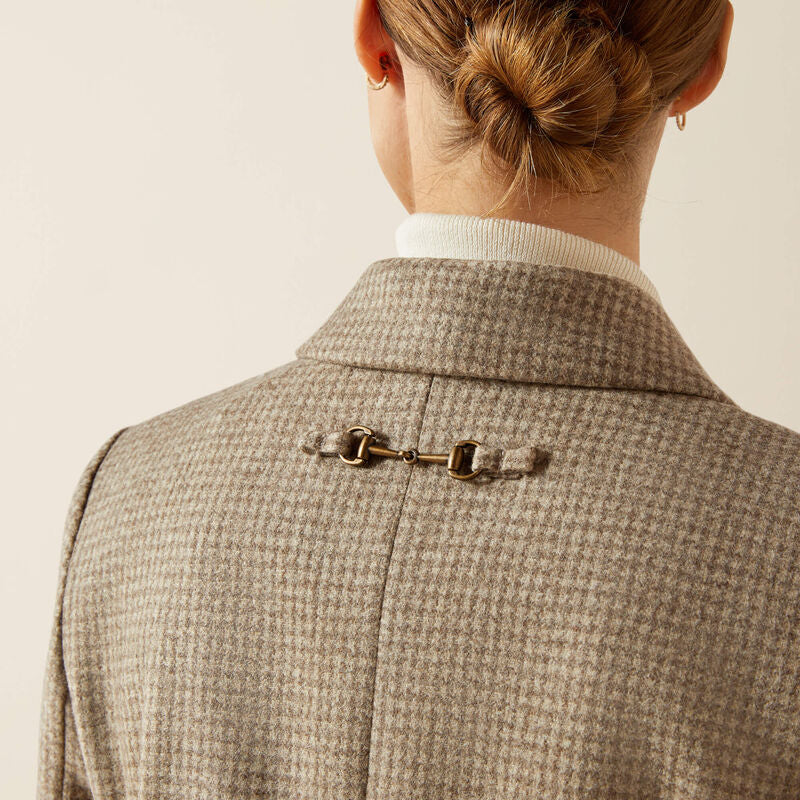 Close-up of a person wearing a textured brown coat with a bit ornament on a beige background