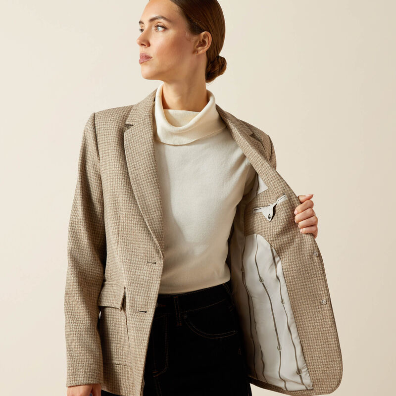 Woman wearing a beige checkered blazer over a white turtleneck with a beige background