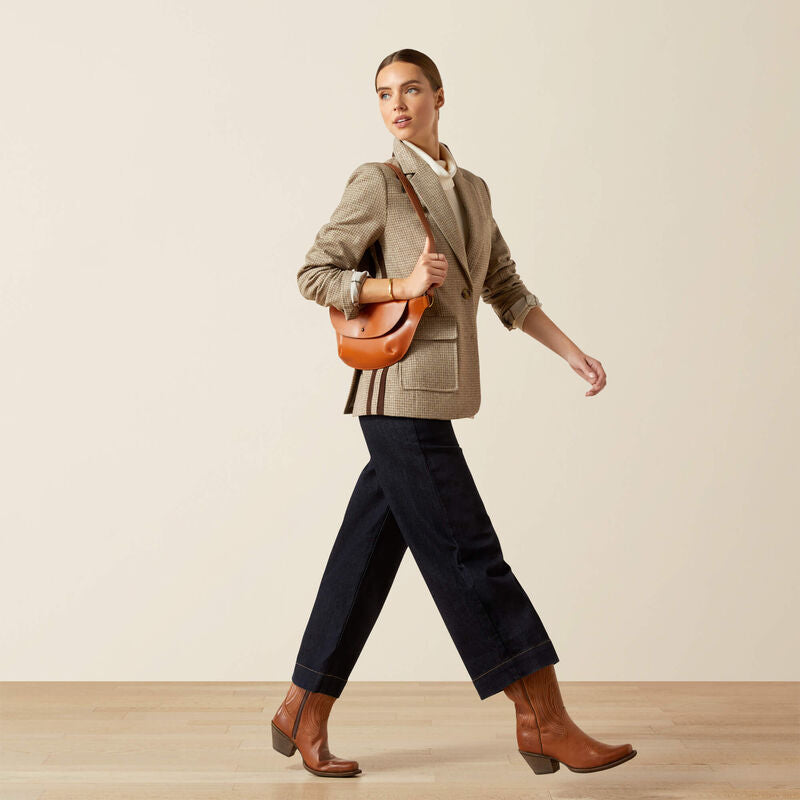 Woman in a beige blazer and brown boots holding an orange handbag on a plain background