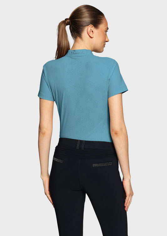 Woman wearing a blue shirt with perforations and black breeches on a beige background