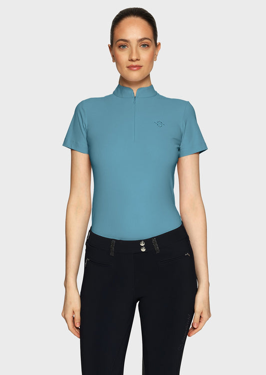 Woman wearing a blue shirt with perforations and black breeches on a beige background