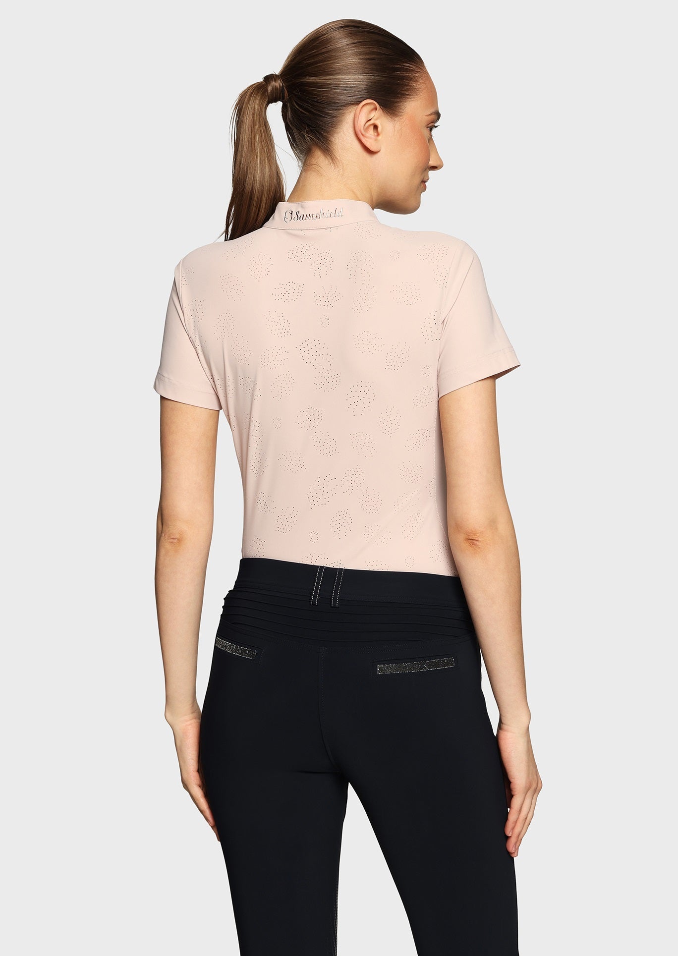 Woman wearing a pink shirt with perforations and black breeches on a beige background