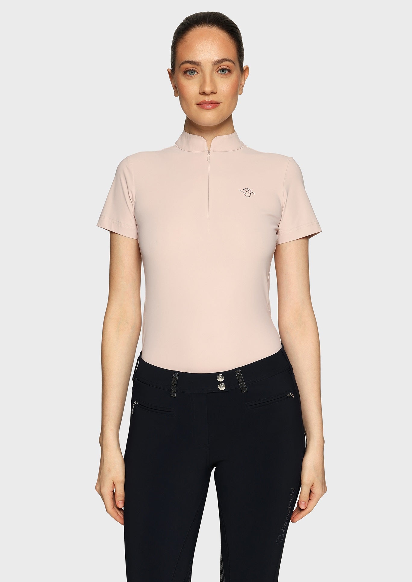 Woman wearing a pink shirt with perforations and black breeches on a beige background