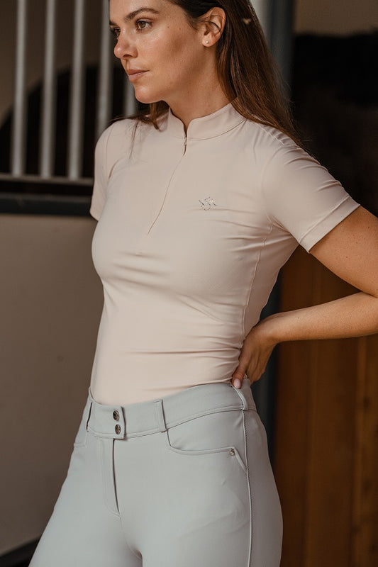 Woman wearing a beige top and light gray pants in an indoor setting