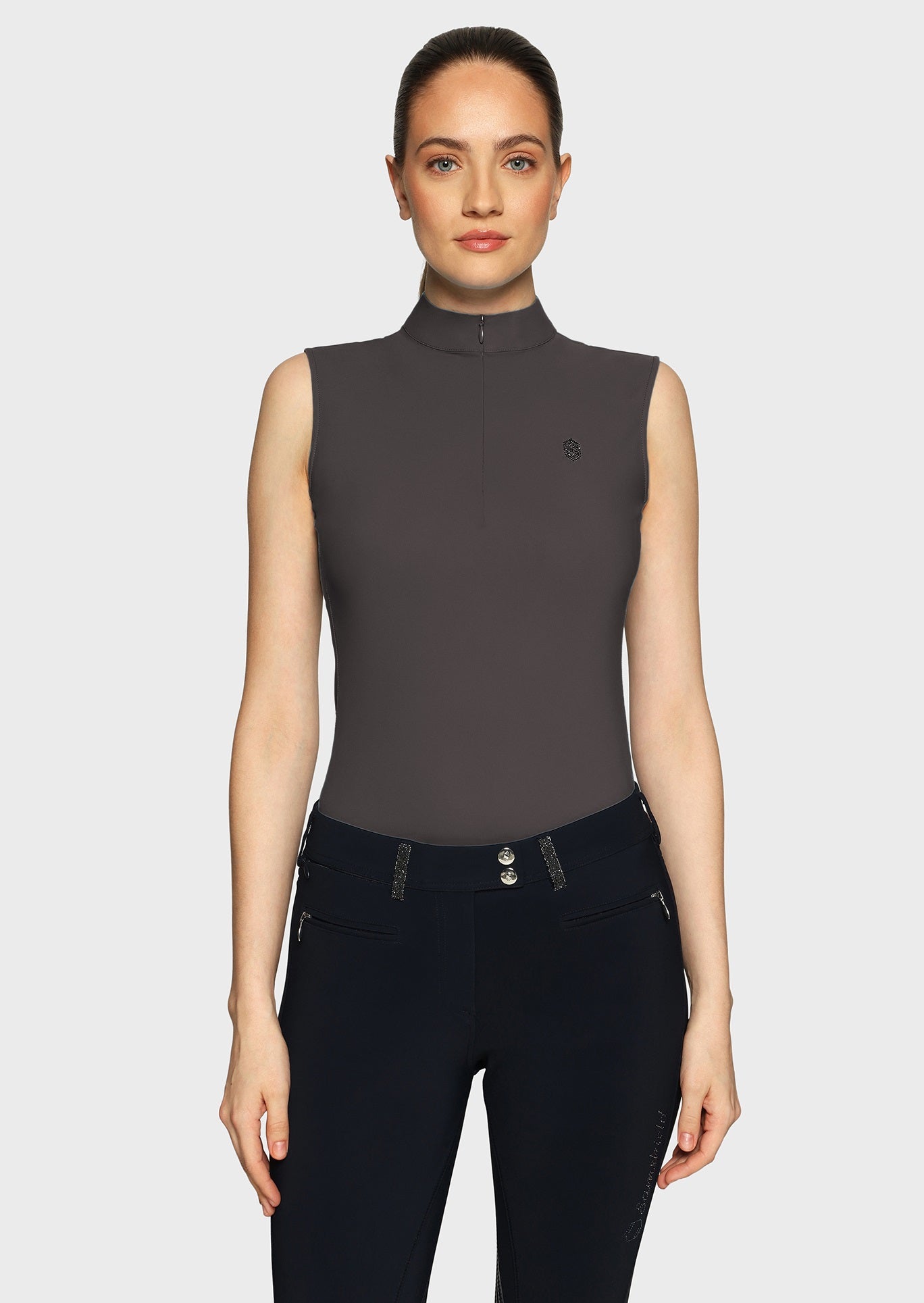 Woman wearing a grey sleeveless top and black breeches on a beige background