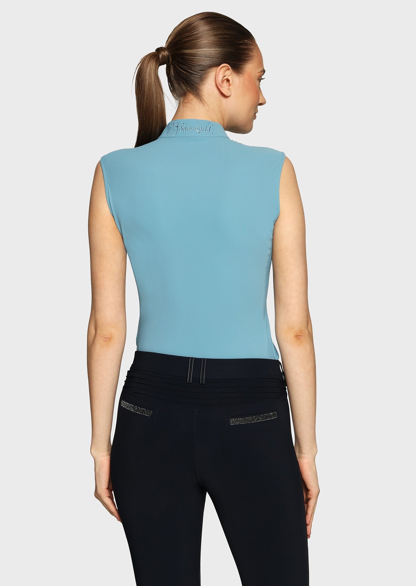 Woman wearing a blue sleeveless top and black breeches on a beige background