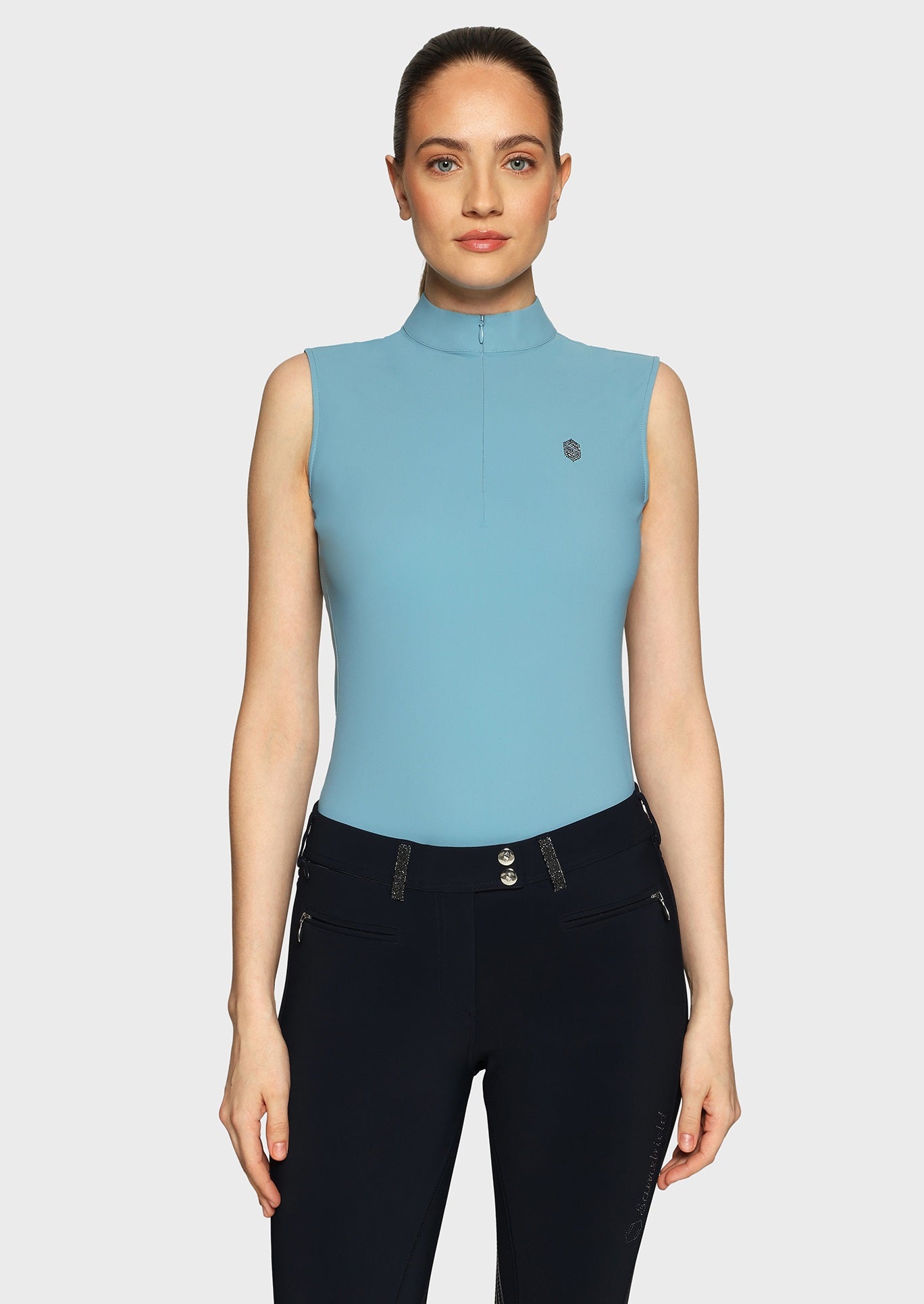 Woman wearing a blue sleeveless top and black breeches on a beige background