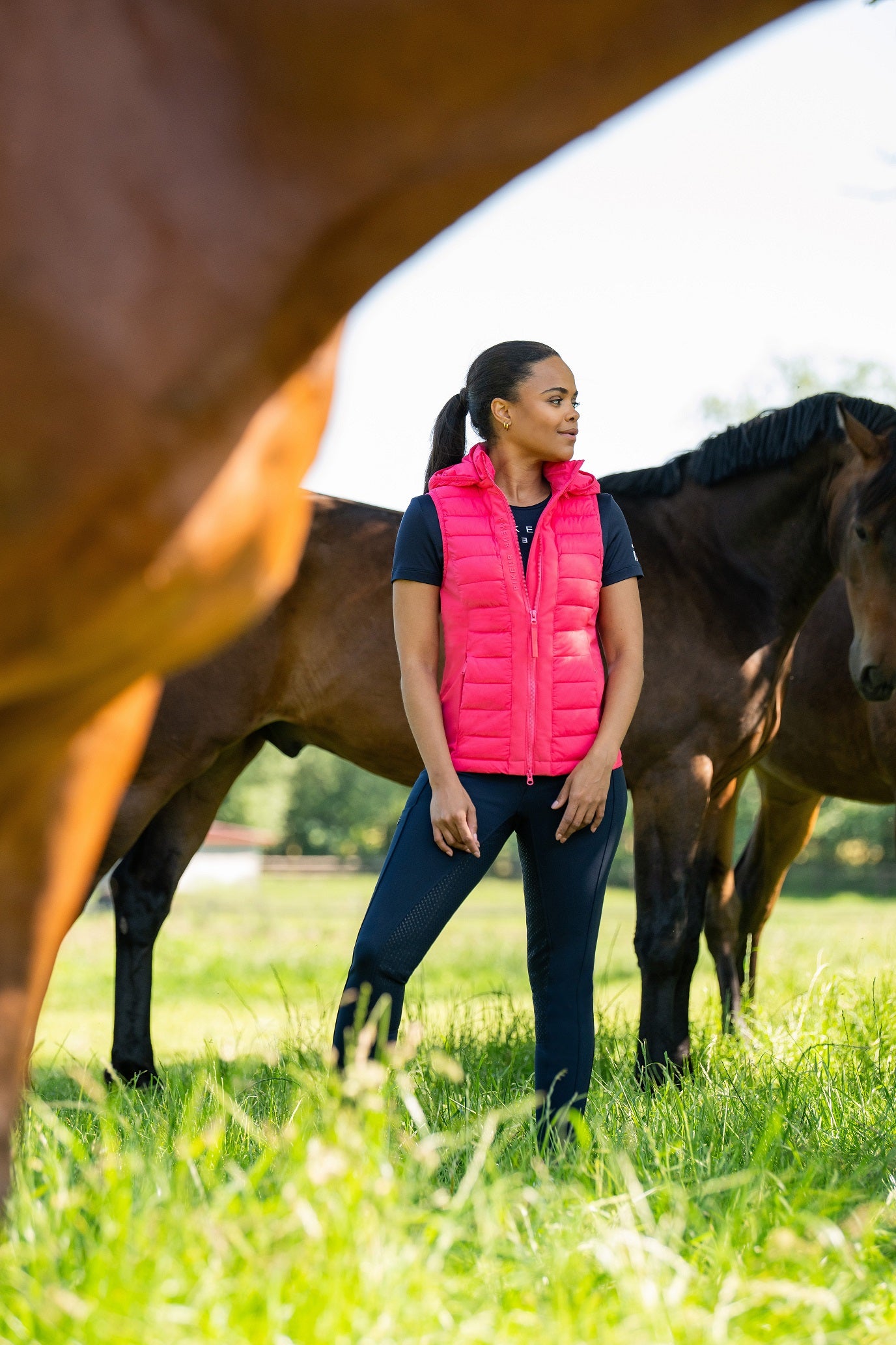 Woman in a pink vest standing next to a horse in a grassy field