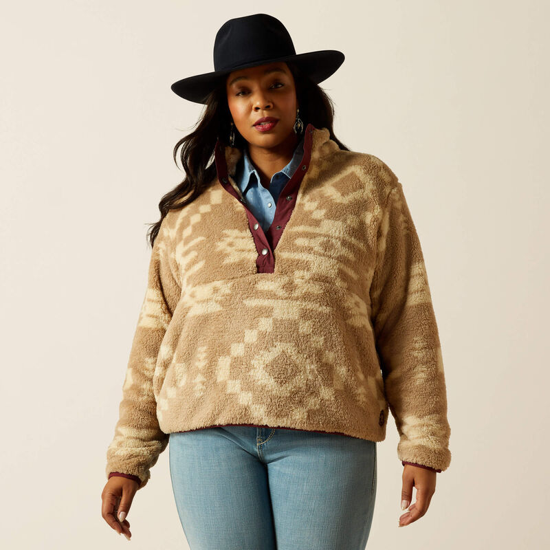 Woman wearing a patterned beige sweater, blue jeans, and a black hat on a beige background