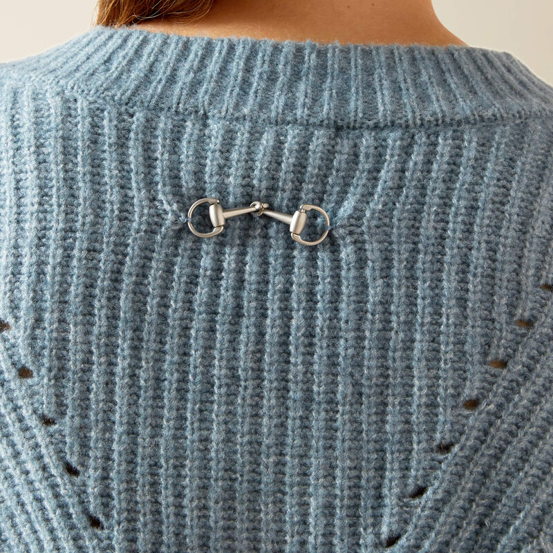 Close-up of a blue knitted sweater with a metallic horse bit brooch.