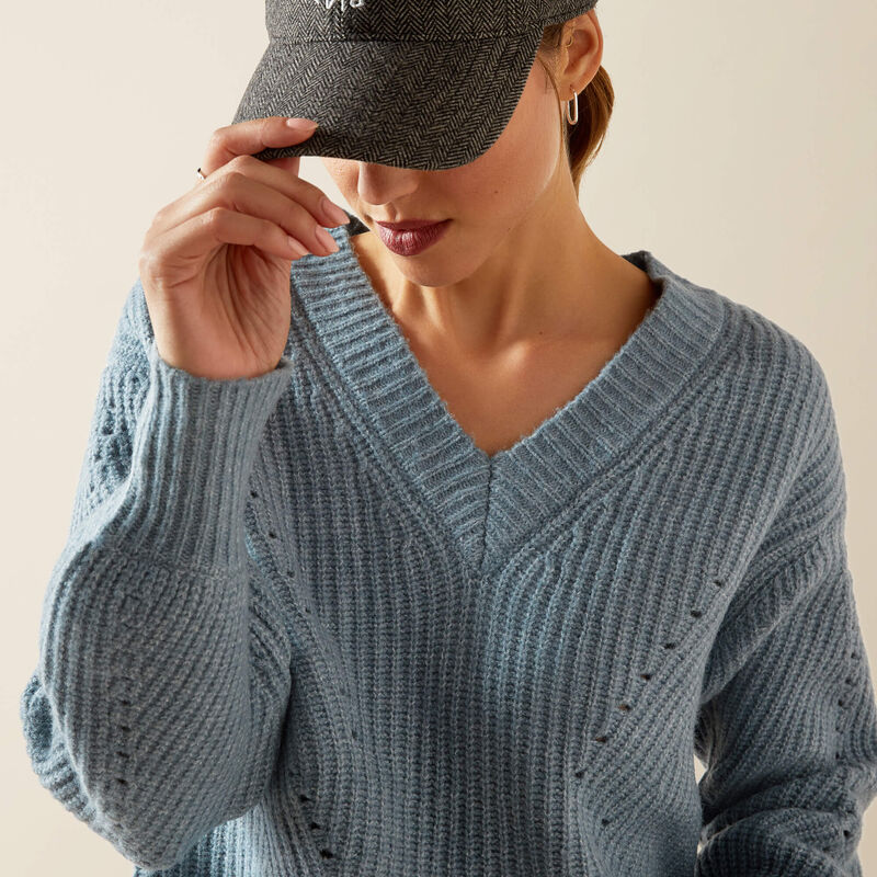 Woman wearing a blue sweater and dark cap against a beige background