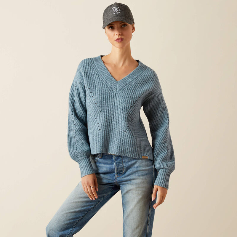 Woman wearing a blue sweater and jeans with a cap on a beige background