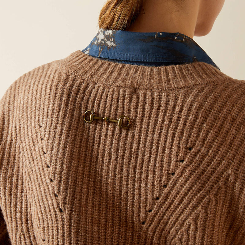 Close-up of a brown knitted sweater with a decorative bit brooch on a neutral background