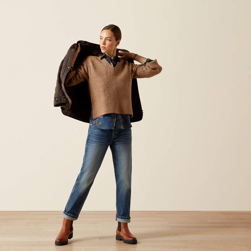 Person wearing a brown sweater, blue jeans, and brown shoes against a plain background