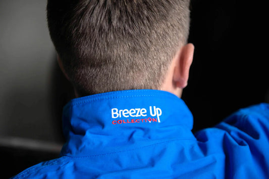 Close-up back view of a person wearing a bright blue jacket, showing the inside of the collar with the embroidered text 'Breeze Up COLLECTION' in white and red.